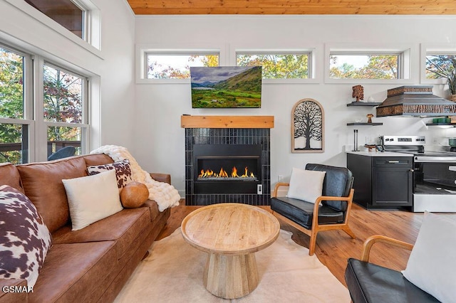 living room with light wood-type flooring, wooden ceiling, and a tiled fireplace