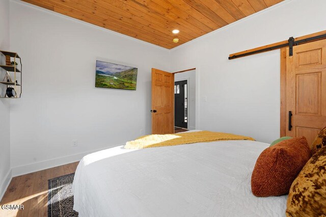 bedroom featuring a barn door, wood-type flooring, wood ceiling, and crown molding