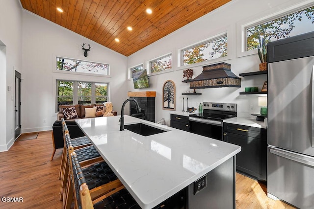 kitchen with light stone countertops, appliances with stainless steel finishes, wood ceiling, sink, and an island with sink