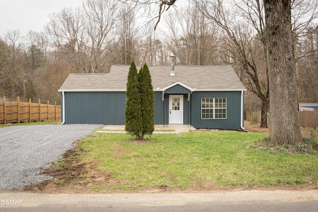 view of front facade featuring gravel driveway, fence, and a front lawn