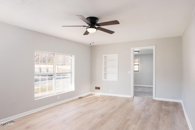 unfurnished bedroom featuring visible vents, baseboards, light wood-style flooring, ceiling fan, and a walk in closet