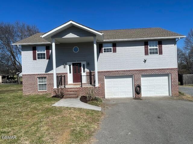 raised ranch with aphalt driveway, brick siding, an attached garage, and a front lawn