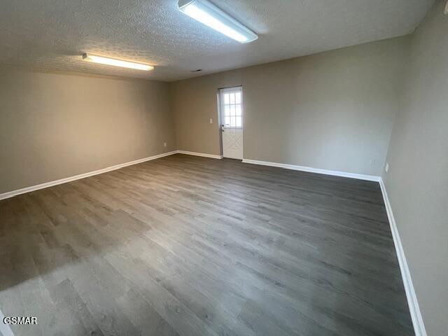 spare room with dark wood-style floors, a textured ceiling, and baseboards