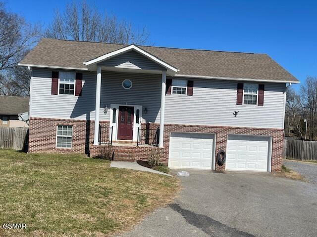 split foyer home with a garage, brick siding, fence, driveway, and a front lawn