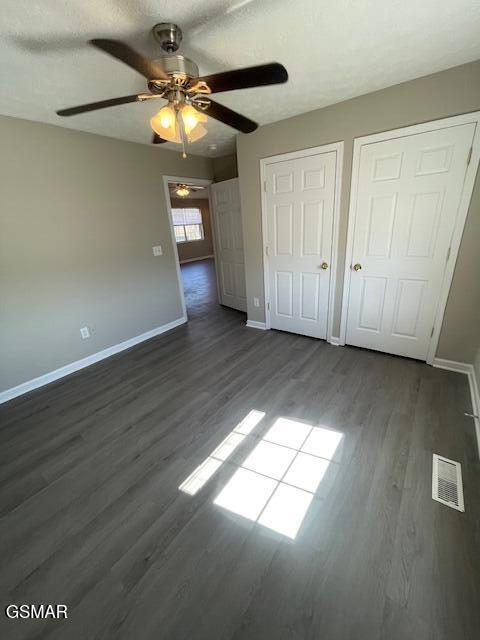 unfurnished bedroom with dark wood-style floors, two closets, visible vents, and baseboards