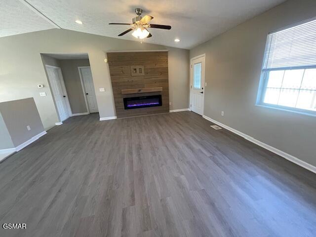 unfurnished living room featuring a large fireplace, dark wood-type flooring, a ceiling fan, baseboards, and vaulted ceiling