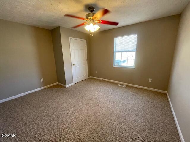 unfurnished bedroom with a textured ceiling, a ceiling fan, visible vents, baseboards, and carpet