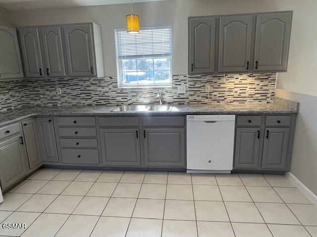 kitchen featuring light stone countertops, gray cabinetry, a sink, decorative backsplash, and dishwasher