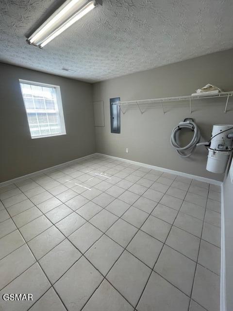 spare room featuring light tile patterned floors, electric panel, baseboards, and a textured ceiling