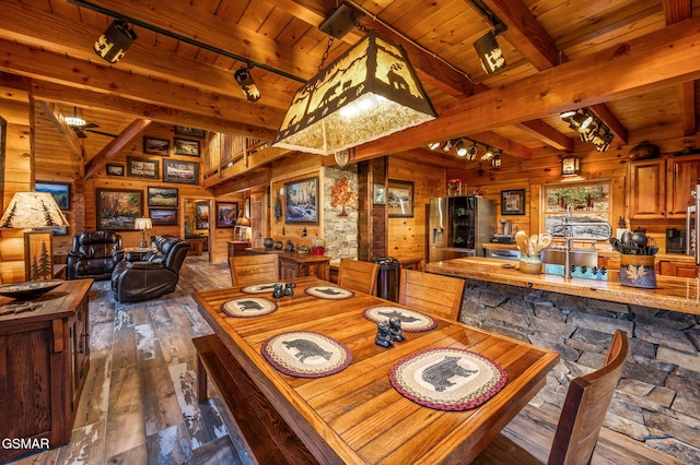 dining room with wooden walls, dark wood-style floors, beam ceiling, track lighting, and wooden ceiling