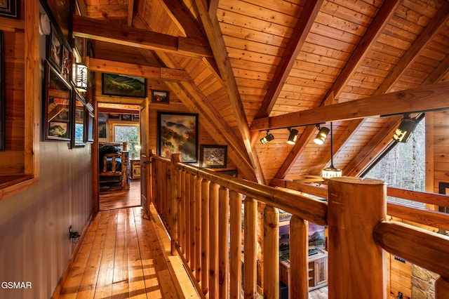 hall featuring light wood-style floors, wood ceiling, wood walls, and vaulted ceiling with beams