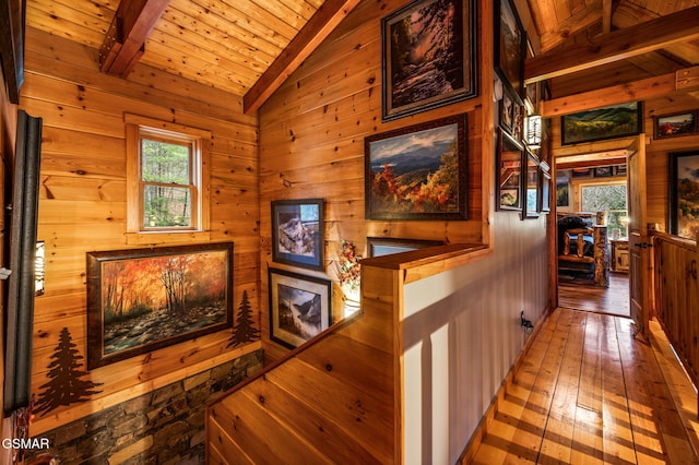 hallway featuring plenty of natural light, wood walls, vaulted ceiling with beams, and hardwood / wood-style flooring