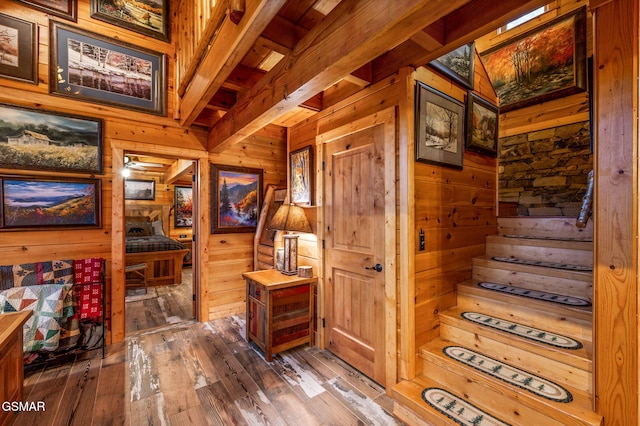 staircase with hardwood / wood-style flooring, wooden walls, and beamed ceiling