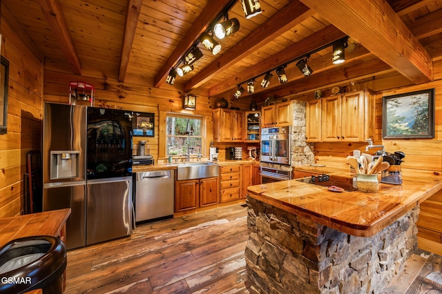 kitchen with hardwood / wood-style flooring, a sink, stainless steel appliances, wooden walls, and wooden ceiling