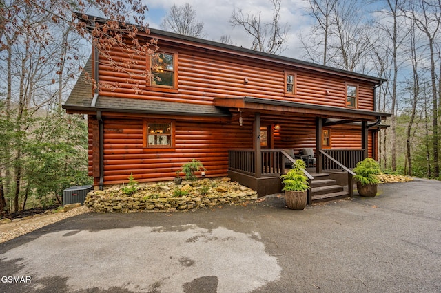 log home featuring central AC unit, covered porch, driveway, and a shingled roof