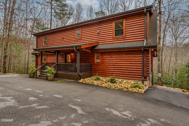 log cabin with aphalt driveway, covered porch, and a shingled roof