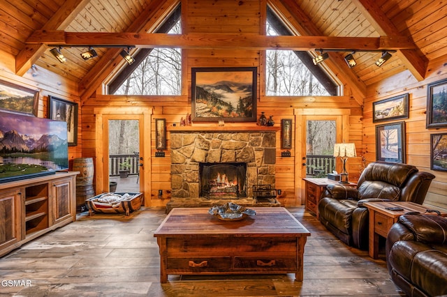 living area with beam ceiling, wood-type flooring, a stone fireplace, wood walls, and wooden ceiling