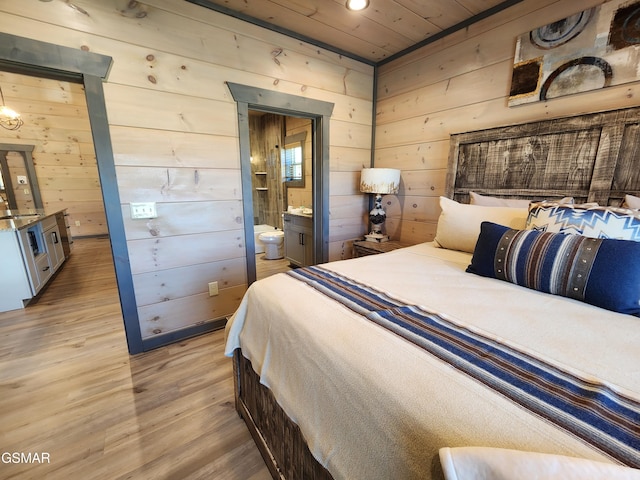 bedroom with connected bathroom, a sink, wood walls, and light wood finished floors