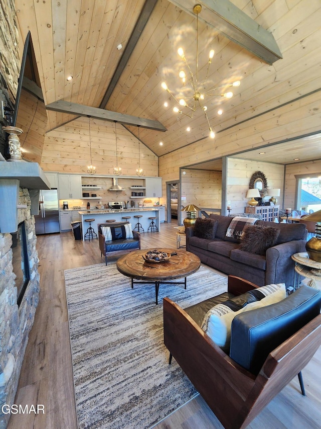living area featuring wood walls, a stone fireplace, wood finished floors, a chandelier, and wooden ceiling