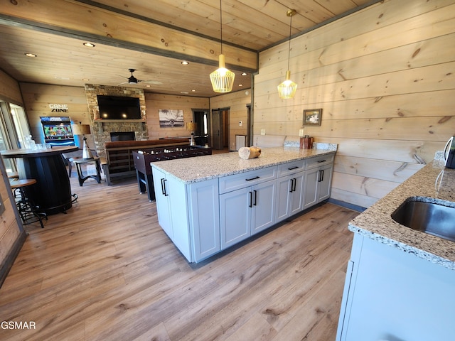 kitchen with wooden walls, wooden ceiling, a peninsula, light stone countertops, and light wood-type flooring