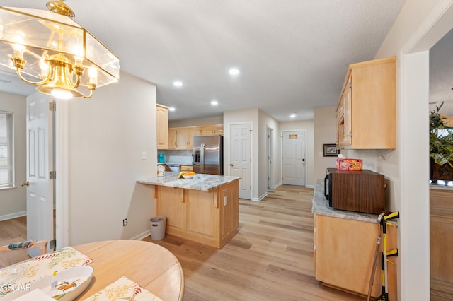 kitchen featuring kitchen peninsula, appliances with stainless steel finishes, light wood-type flooring, light brown cabinets, and a notable chandelier