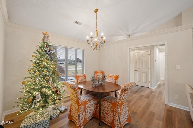 dining area with ornamental molding, wood-type flooring, a textured ceiling, and an inviting chandelier