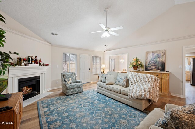 living room with ceiling fan, lofted ceiling, a textured ceiling, and light hardwood / wood-style flooring