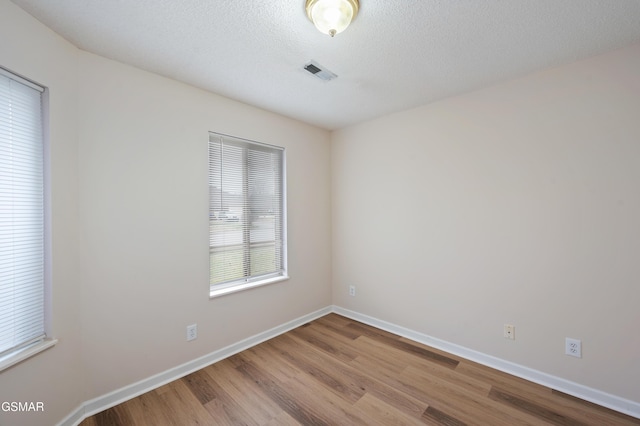 spare room featuring a textured ceiling, light wood-type flooring, and a wealth of natural light