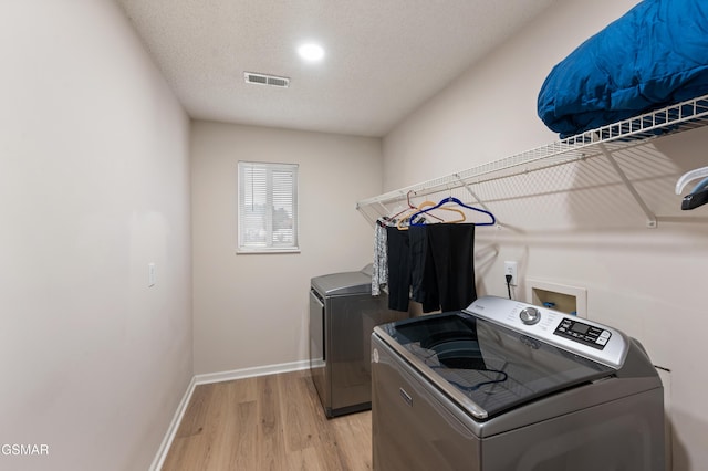 laundry area with light hardwood / wood-style floors, washing machine and dryer, and a textured ceiling