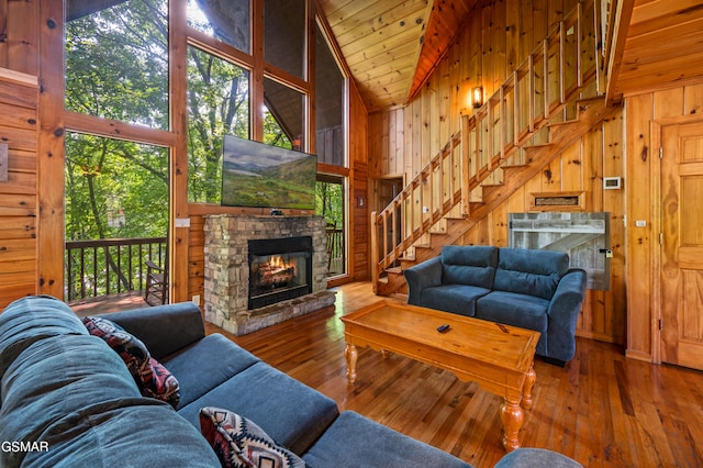 living room featuring a fireplace, high vaulted ceiling, wooden walls, stairs, and hardwood / wood-style floors