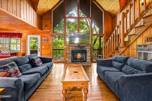 living room with wooden walls, high vaulted ceiling, wood-type flooring, wood ceiling, and a stone fireplace