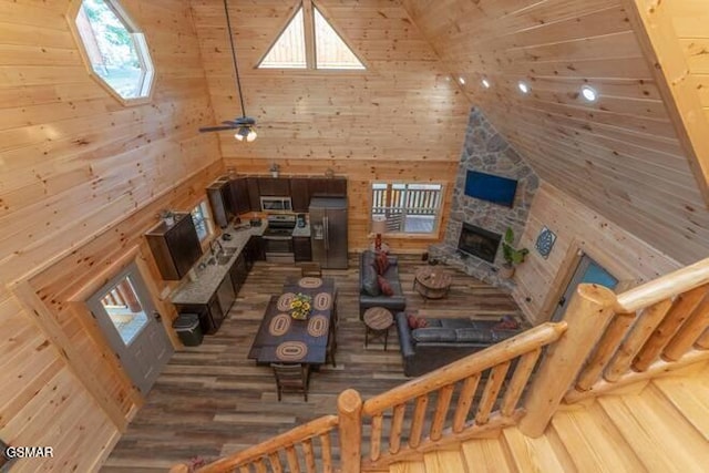 living room with ceiling fan, hardwood / wood-style floors, high vaulted ceiling, and wooden walls