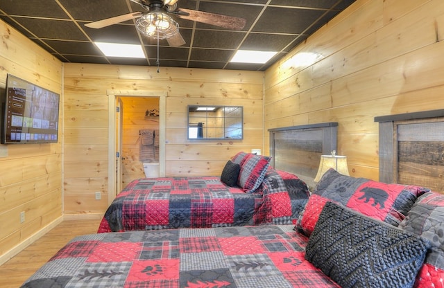 bedroom with ceiling fan, a drop ceiling, and wooden walls