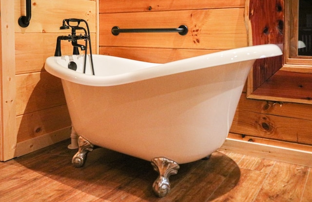 bathroom featuring hardwood / wood-style flooring, a tub, and wooden walls