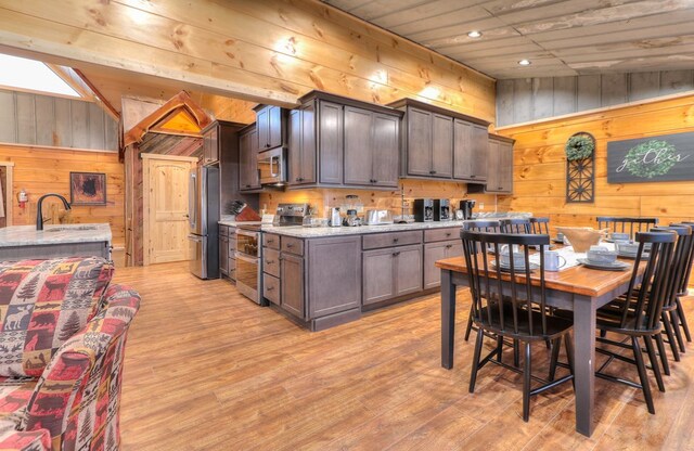 kitchen featuring dark brown cabinets, wood walls, and stainless steel appliances