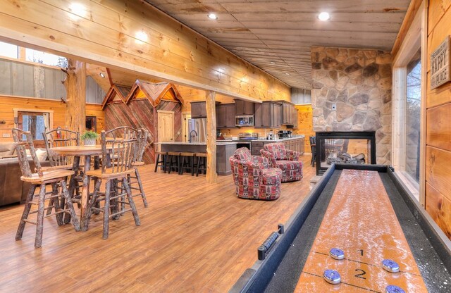 playroom with wooden walls, light hardwood / wood-style flooring, a stone fireplace, and wooden ceiling