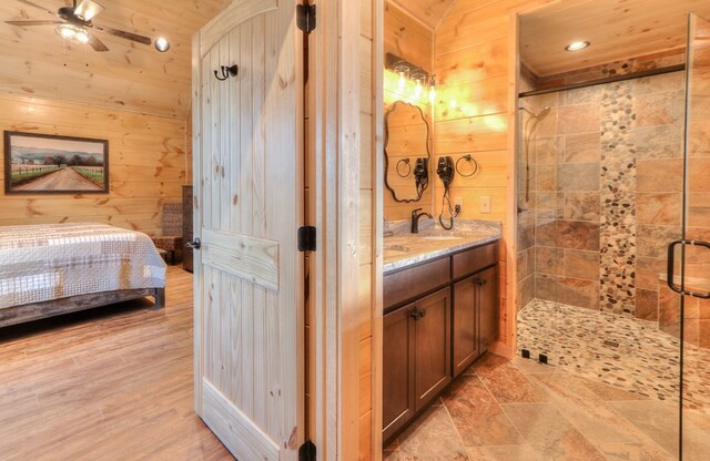 bathroom featuring vanity, a shower with door, wooden walls, ceiling fan, and wood ceiling