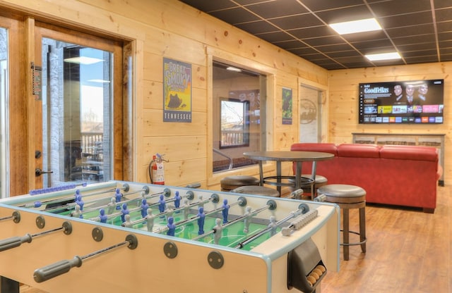 game room with a paneled ceiling, wood walls, and wood-type flooring