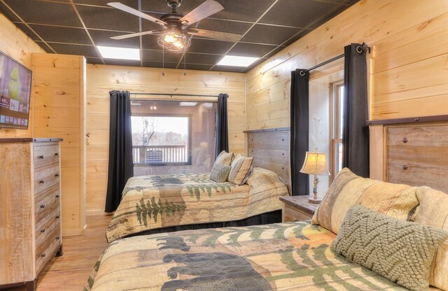 bedroom featuring ceiling fan, light wood-type flooring, a drop ceiling, and wood walls