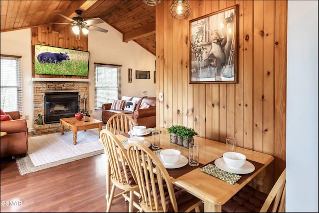 dining space with wood ceiling, ceiling fan, wooden walls, hardwood / wood-style floors, and a stone fireplace