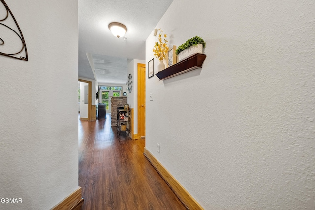 hall featuring baseboards, a textured wall, and dark wood-style flooring