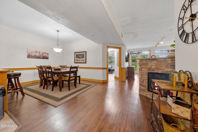 dining room with baseboards, a fireplace, wood finished floors, and track lighting