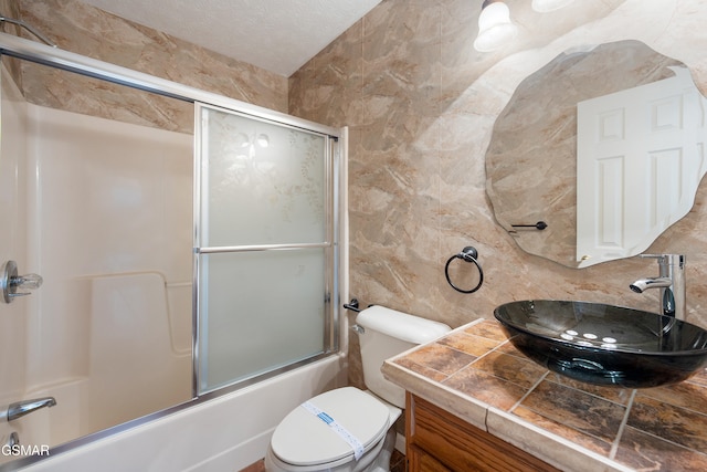 full bathroom featuring combined bath / shower with glass door, toilet, tile walls, and vanity