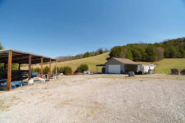 view of yard featuring a rural view, a detached garage, and an outbuilding