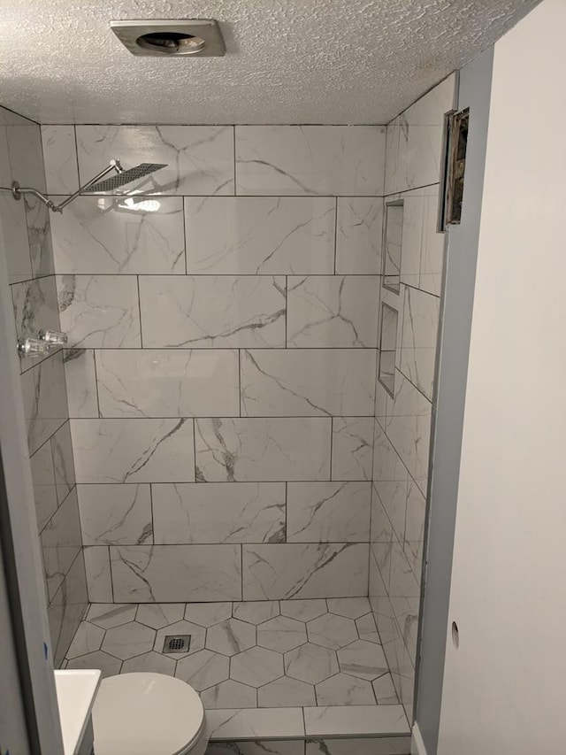 bathroom with a textured ceiling, toilet, and tiled shower