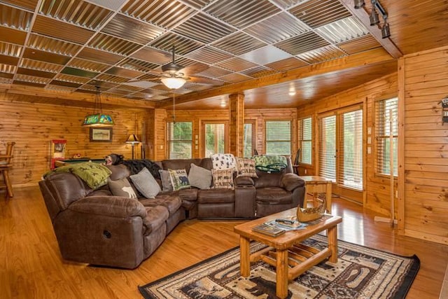 living room with ceiling fan, light wood-type flooring, and wooden walls