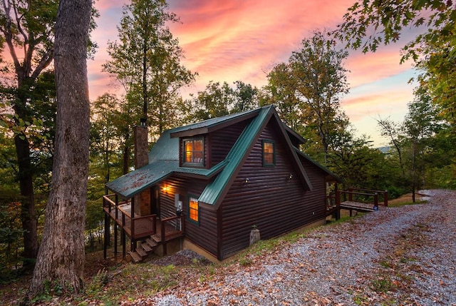 rear view of house with metal roof, a chimney, driveway, and faux log siding