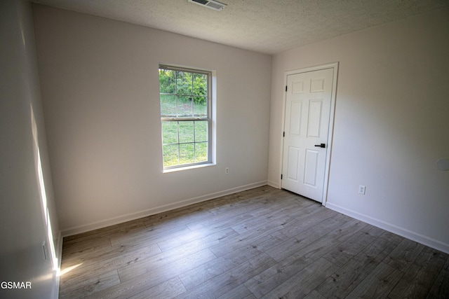 unfurnished room featuring visible vents, baseboards, wood finished floors, and a textured ceiling
