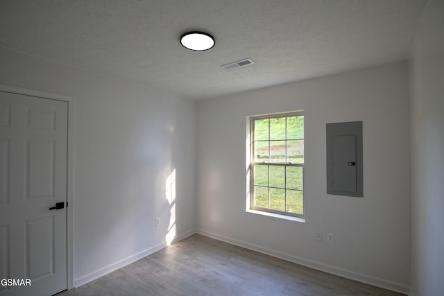 unfurnished room featuring baseboards, electric panel, a textured ceiling, visible vents, and wood finished floors