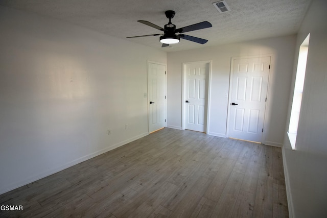 unfurnished bedroom featuring two closets, wood finished floors, baseboards, and visible vents